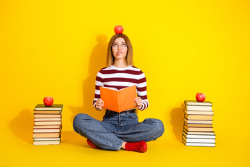 Young woman seated with book on a vibrant yellow background holding an open book, displaying a...