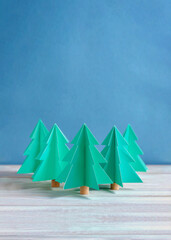 Trendy Nordic DIY homemade style folded paper Christmas tree decorations on a wooden table against a blue background for background, wallpaper, poster, holiday invite, Christmas card.