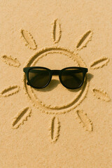 Sunglasses Centered in a Hand-Drawn Sun Illustration on Golden Beach Sand in a Top-Down Artistic Composition