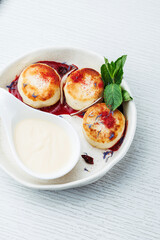 Close up dessert on white plate with mint leaves. Elegant breakfast with cottage cheese pancakes, berry sauce, and cream