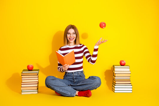 Young woman sitting with book on yellow background, reading a book, holding an apple, cheerful and casual style