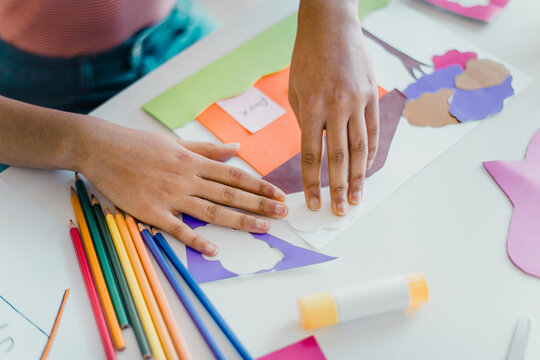 Hands working on a creative craft project with colorful paper and pencils, showcasing an artistic and educational activity