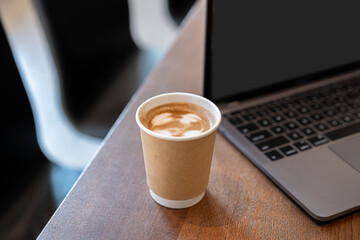 Close-up of Hot coffee latte with latte art milk foam in cup made of paper and laptop computer on wood desk office desk in coffee shop at the cafe,during business work concept