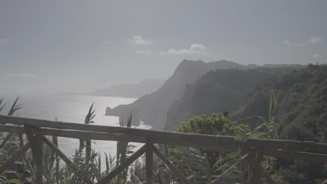 Wooden railing overlooks sunlit cliffs and shimmering Atlantic off Madeira island (SLOG3)