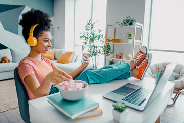 Young woman enjoying leisure time indoors, sitting comfortably with headphones, relaxing, enjoying snack