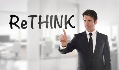 Businessman touching "Rethink" text on transparent wipe board in an office	
