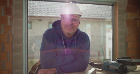 Construction worker smiling confidently at workbench in building under construction, wearing safety helmet, relaxed and professional atmosphere on construction site