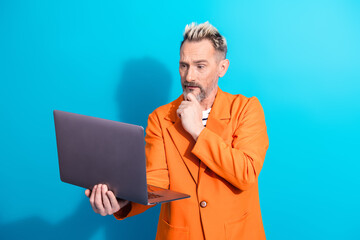 Stylish mature gentleman in an orange blazer using a laptop against a vibrant blue backdrop, showcasing modern technology and elegance