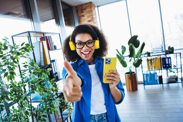 Young businesswoman with headphones pointing enthusiastically in a modern office setting with...
