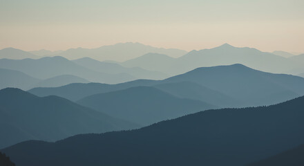 A serene and atmospheric landscape captures successive layers of rolling mountain ridges, fading into the distant horizon under a soft, hazy sky