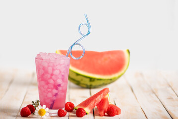 Glass with ice and raspberry and watermelon soda, with fruit pieces on a white wooden table, copy space.