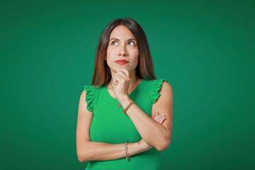 Young Latina woman with black hair and green shirt in expression of thought and doubt, on a vibrant...