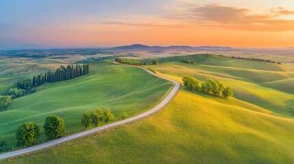 Obraz premium Scenic road through rolling hills at sunset with lush green fields and trees