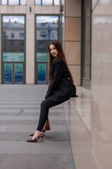 A beautiful girl in a black jacket and leggings against the backdrop of city streets.
