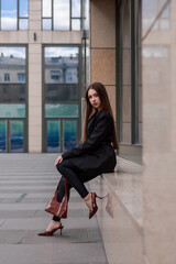 Obraz premium A beautiful girl in a black jacket and leggings against the backdrop of city streets.