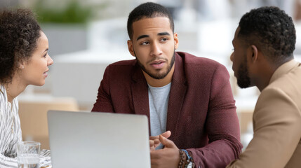 Diverse colleagues converse at a table, a laptop between them, during discussion