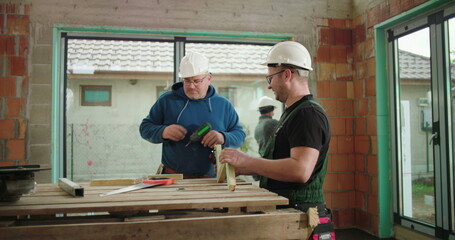 Construction workers examining and aligning wood piece on construction site, both wearing helmets, teamwork in building structure, focus on precision and safety