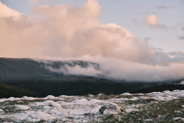 Misty mountain landscape at sunrise. Soft pink clouds drift over a snow-dusted hillside, creating a serene and peaceful atmosphere. Perfect for nature, travel, or winter themes.