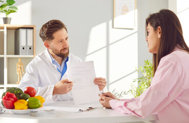 Doctor nutritionist consults with a patient in hospital office, creating a diet and meal plan. The...