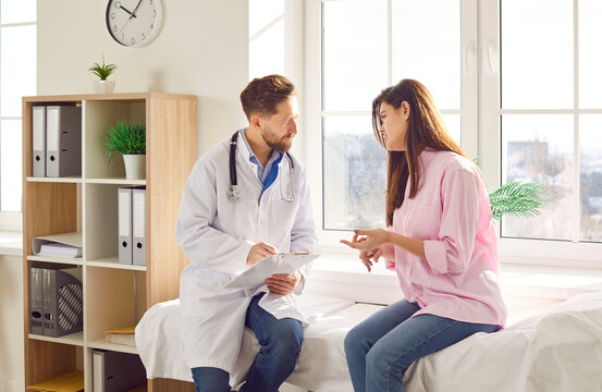 Male doctor, man consulting female patient for treatment, rehabilitation, regular health check up. Physical therapist in medical clinic room listening to woman couch sitting, describing symptoms