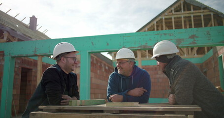 Construction workers in hard hats sharing a lighthearted moment while discussing project plans at a...