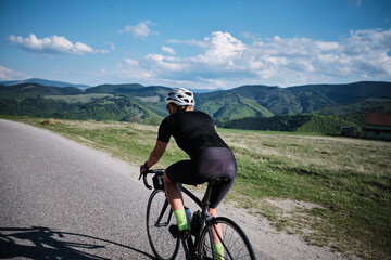 Fototapeta premium Cyclist enjoying a scenic ride through rolling hills and lush green countryside. Perfect for travel, sports, and active lifestyle themes.
