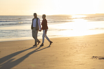 Senior couple walking on the beach at sunset, holding hands