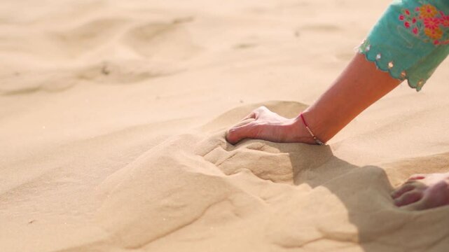 Close up shot of Indian girl grab sand in desert and dropping it at Thar desert in Jaisalmer, Rajasthan, India. Copy space with desert background.