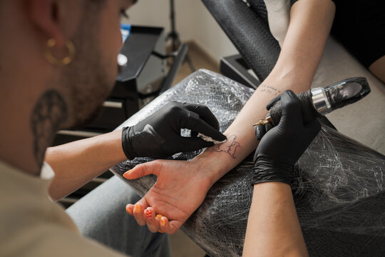 Tattoo artist drawing a tattoo on a customer's arm and cleaning it