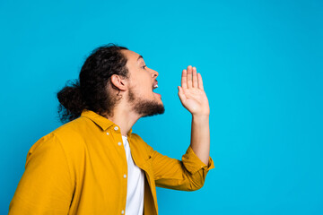 Man in yellow shirt gesturing while speaking against a vivid blue background