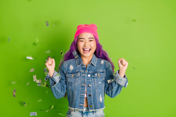 Cheerful young woman with vibrant purple hair and pink beanie in denim jacket celebrating...