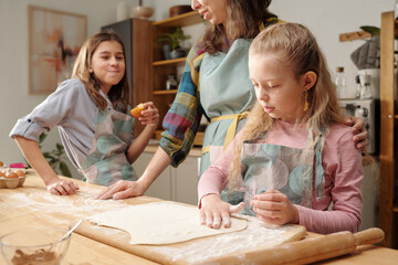 Mother and two daughters baking together, rolling dough on kitchen counter. Family enjoying quality...