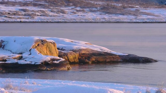 Drone footage shows rocky coastal cliffs in Larvik, Norway, partially snow-covered and glowing in sunrise or sunset light during winter season.