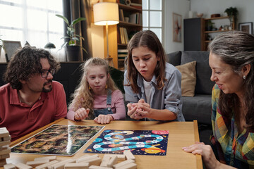 Family sitting around table in living room, playing board games together and enjoying quality time....