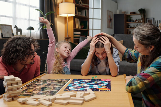 Family gathered around table, celebrating a win during competitive board game night, with expressions of joy and camaraderie evident. Homey background filled with cozy details