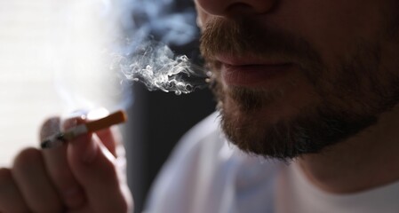 Man smoking cigarette on blurred background, closeup