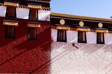 Traditional Tibetan architecture of Gomang Monastery in Amdo, featuring vivid red and white walls, ornate window awnings, and golden medallions, bathed in striking natural light.