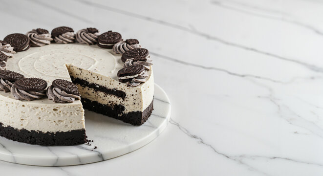 Whole Oreo cookies and cream cheesecake on marble surface with copy space