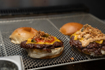 Close-Up of Two Juicy Smash Burgers Being Assembled with Cheese, Pickles, and Sauces on Grill Tray