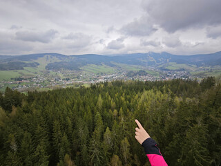 Female hand pointing into dark clouds above hilly landscape with forests