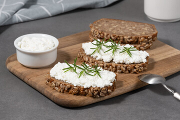 Delicious rye bread topped with creamy cheese and fresh herbs on a rustic wooden board