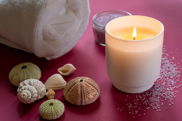 Spa composition. White towel, bath salt, candle, seashells and on a dark pink background. 