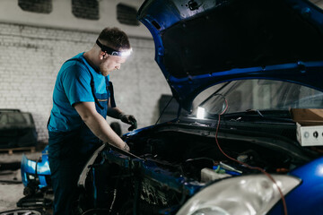young male auto mechanic repairing car in auto service with open hood