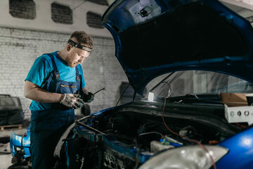 young male auto mechanic repairing car in auto service with open hood