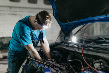 young male auto mechanic repairing car in auto service with open hood