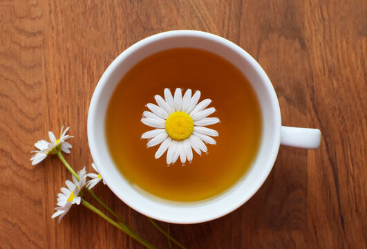 Chamomile medicinal tea in white cup on wooden table with chamomile flowers. Top view.