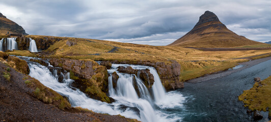 Panoramic view of Famous Kirkjufell mountain with Kirkjufellsfoss infront of it under morning sun light in Iceland during spring time.