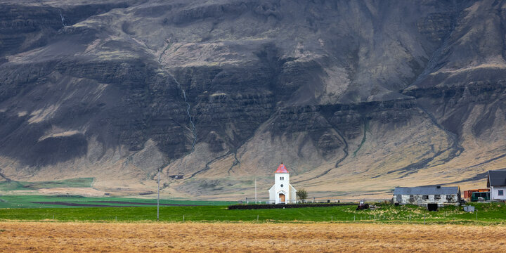 Historic church in scenic landscape of Iceland with tall mountains in the background during spring time..