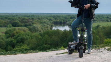 Young man on powerful electric scooter on hill with view of green forest. summer lifestyle, copy space