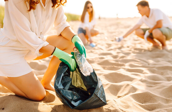 Young friends actively participate in beach cleanup. Cheerful volunteers collect plastic waste and trash along the coastline at sunset. The concept of ecology, ecology and recreation.